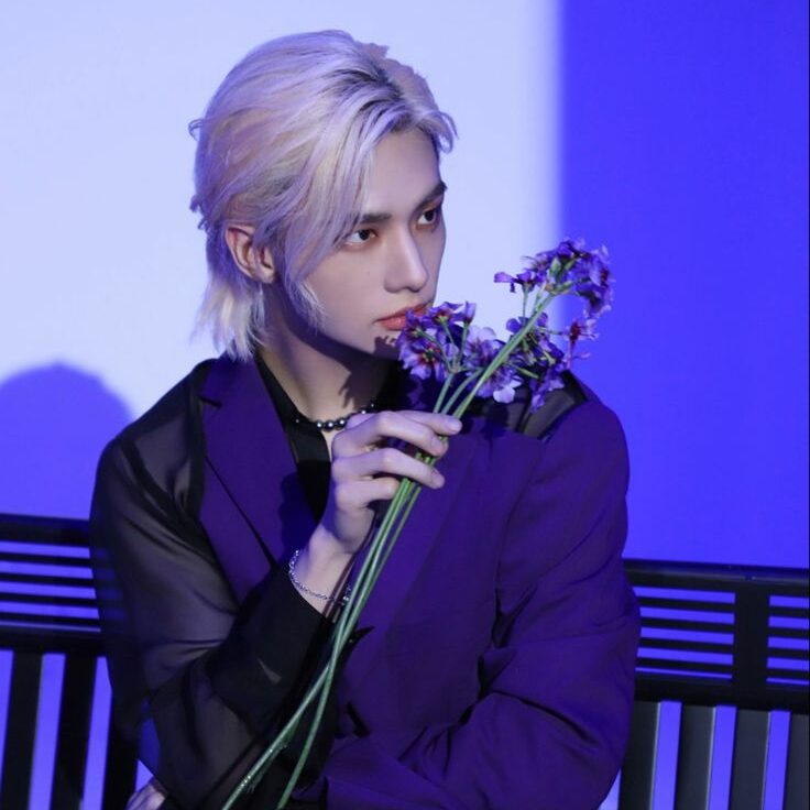 hyunjin of straykids with blonde hair posing with purple flowers against face